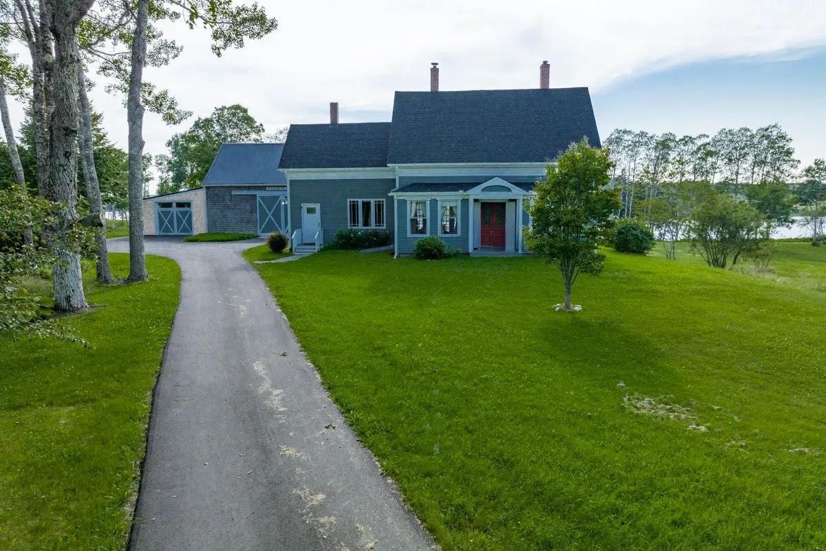 Blue barn and garage with gravel driveway approaching the property