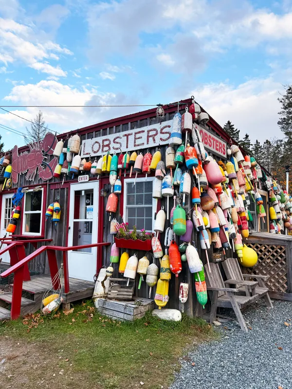Colorful lobster shack covered in buoys with Lobsters sign out front