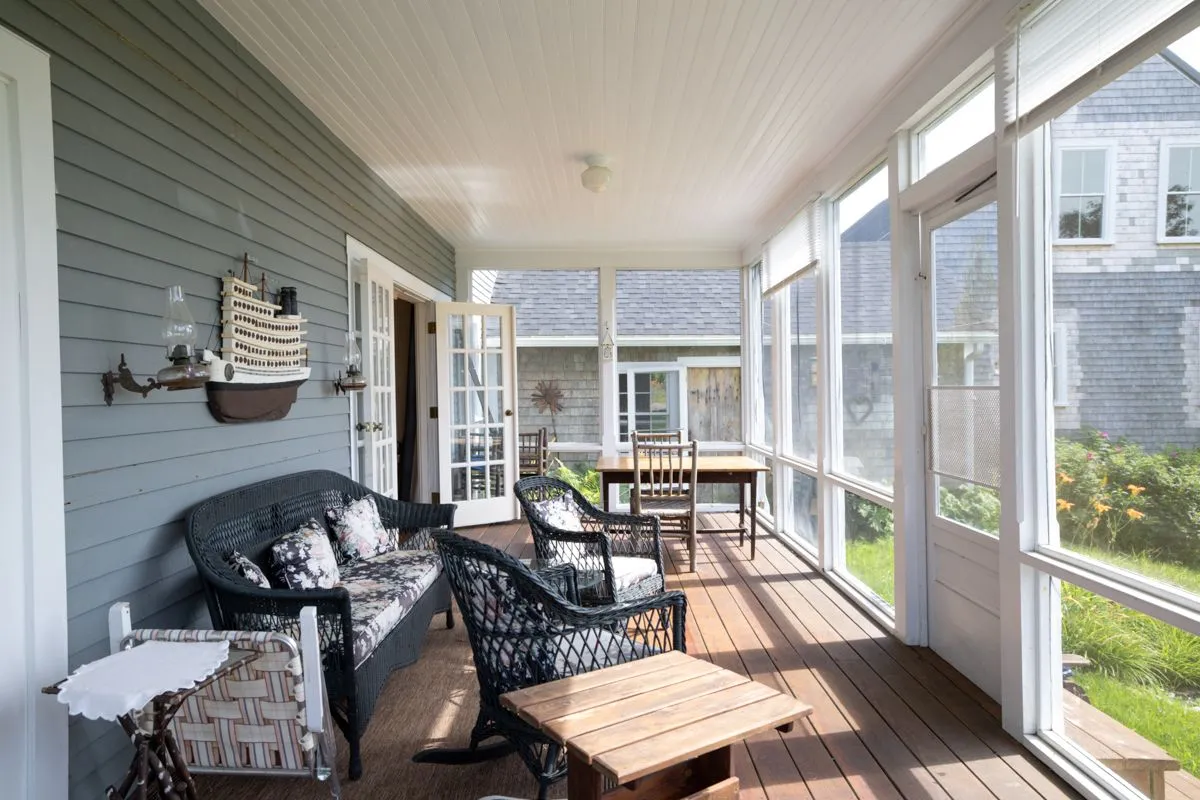 Screened porch with wicker furniture and view of neighboring cottage