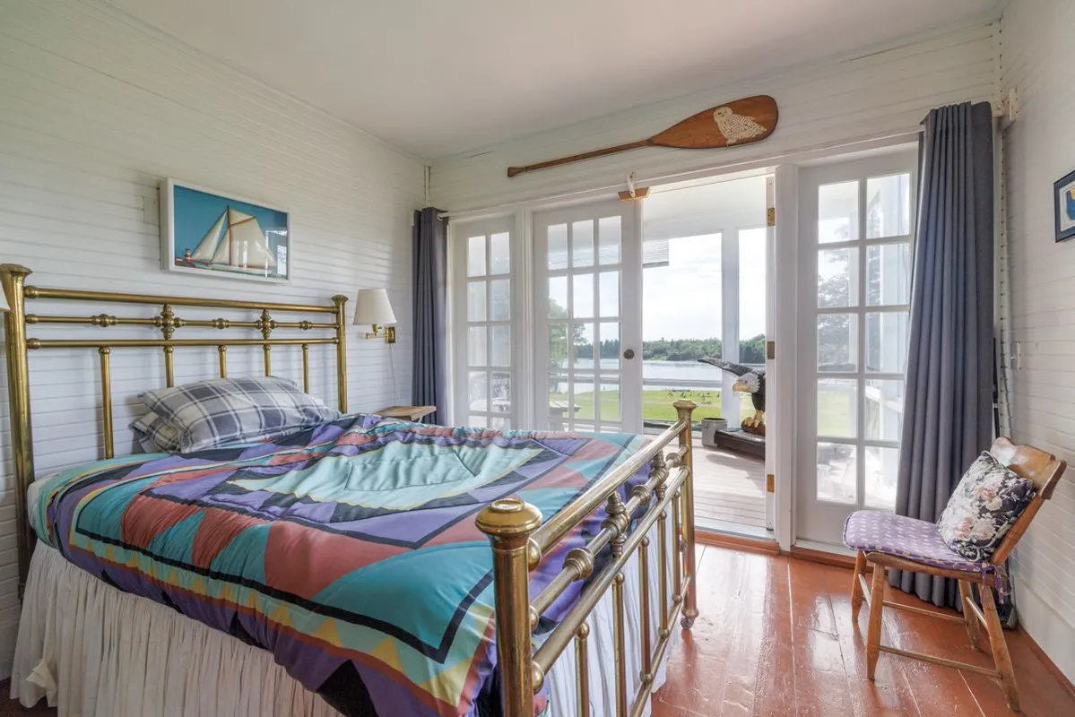 Bright bedroom with brass bed, colorful quilt, and large water-view windows