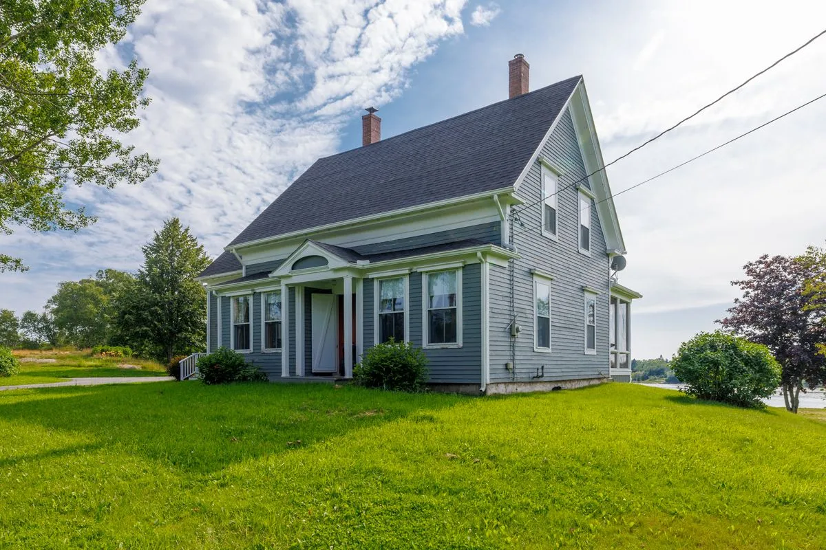 Classic gray New England farmhouse with green lawn on sunny day