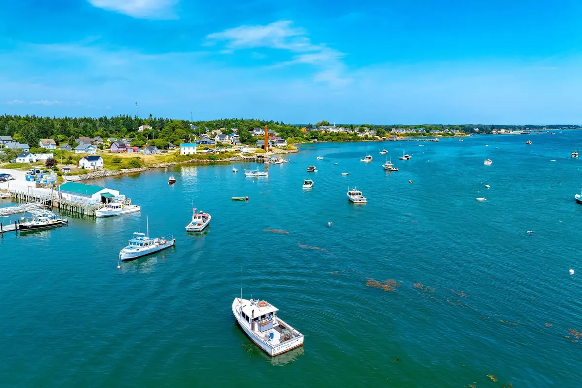Aerial view of turquoise harbor filled with lobster boats near coastal village